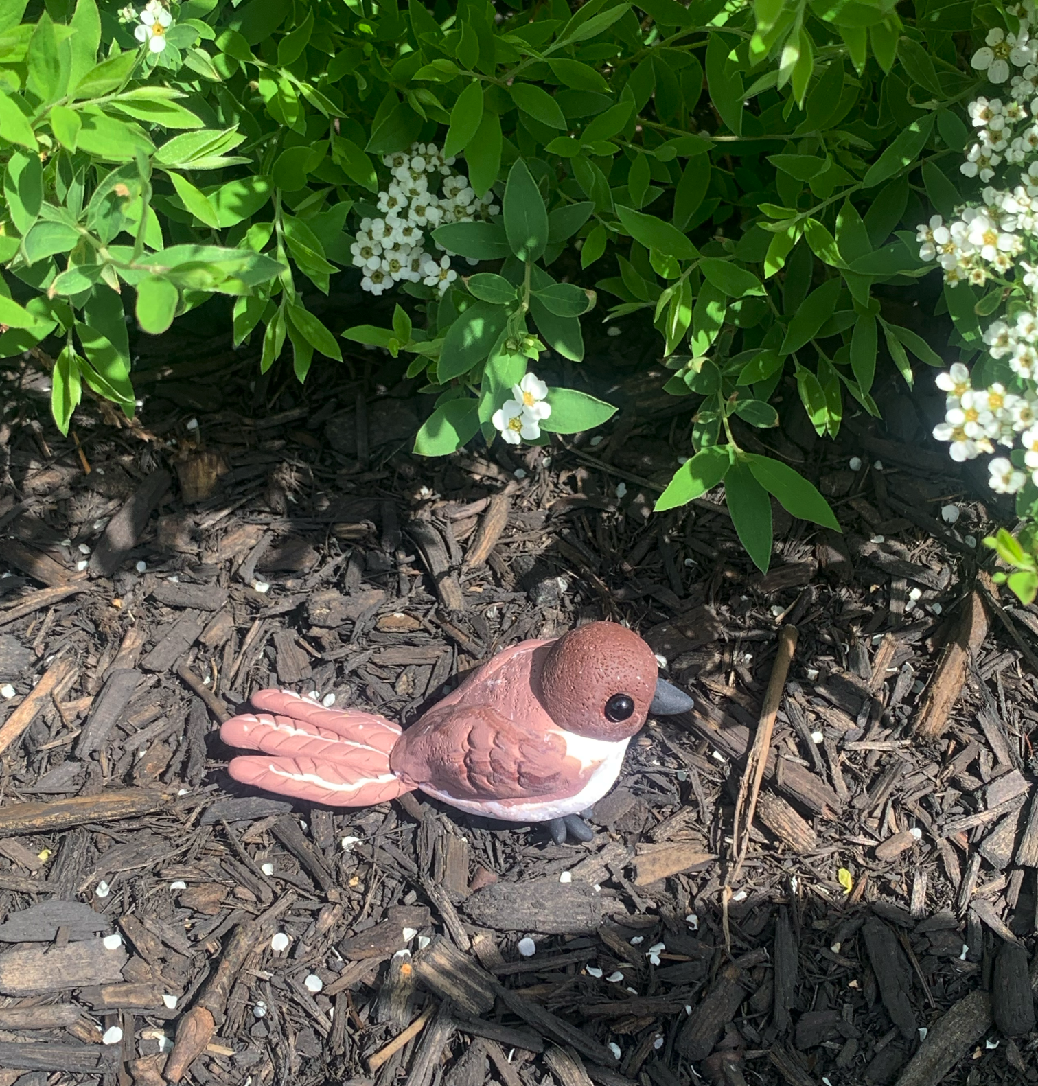 Clay Phoebe sculpture in a garden, side view, sitting in mulch