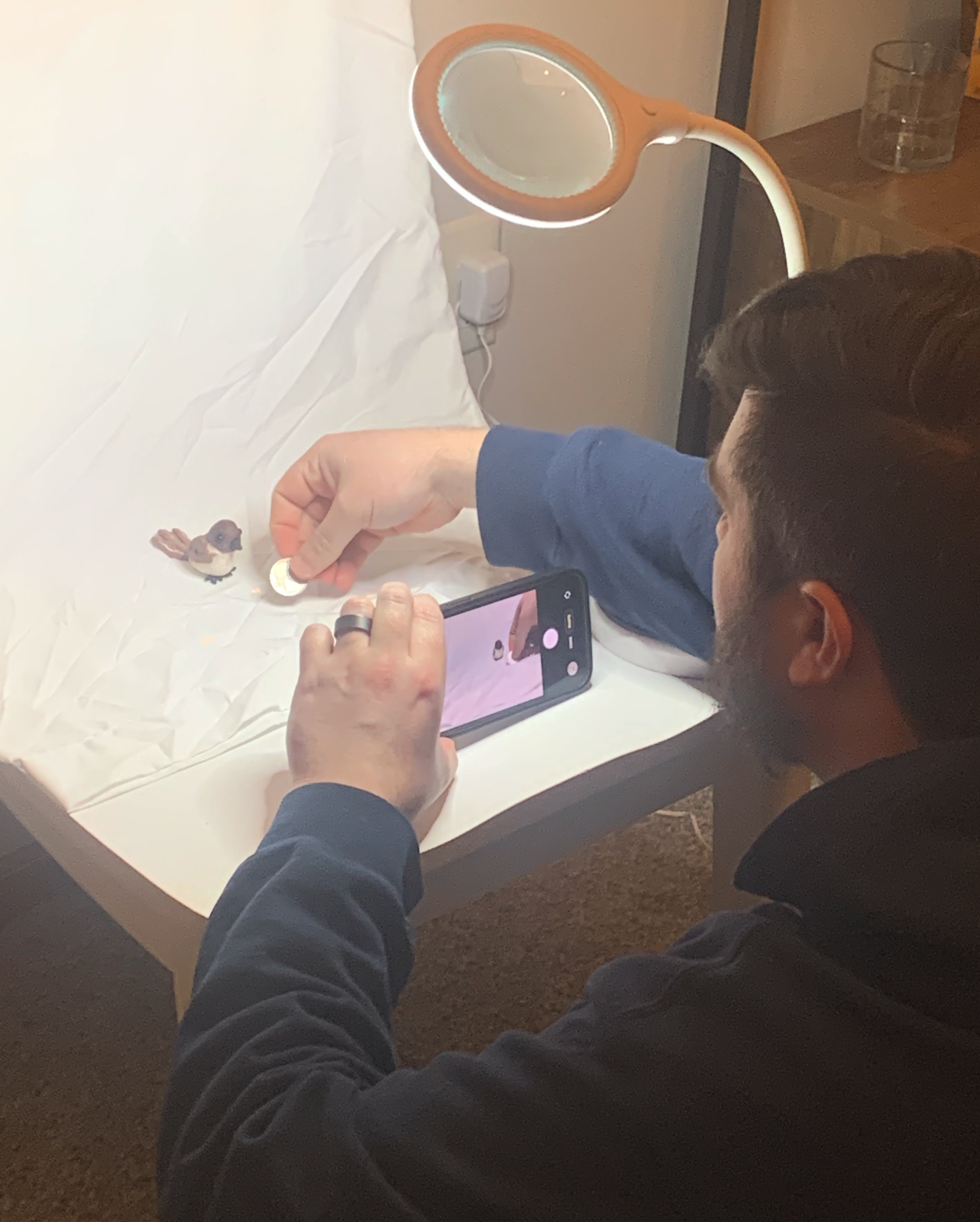 Brother-in-law photographing clay Phoebe on a bedsheet with a magnifying lamp and coin for scale