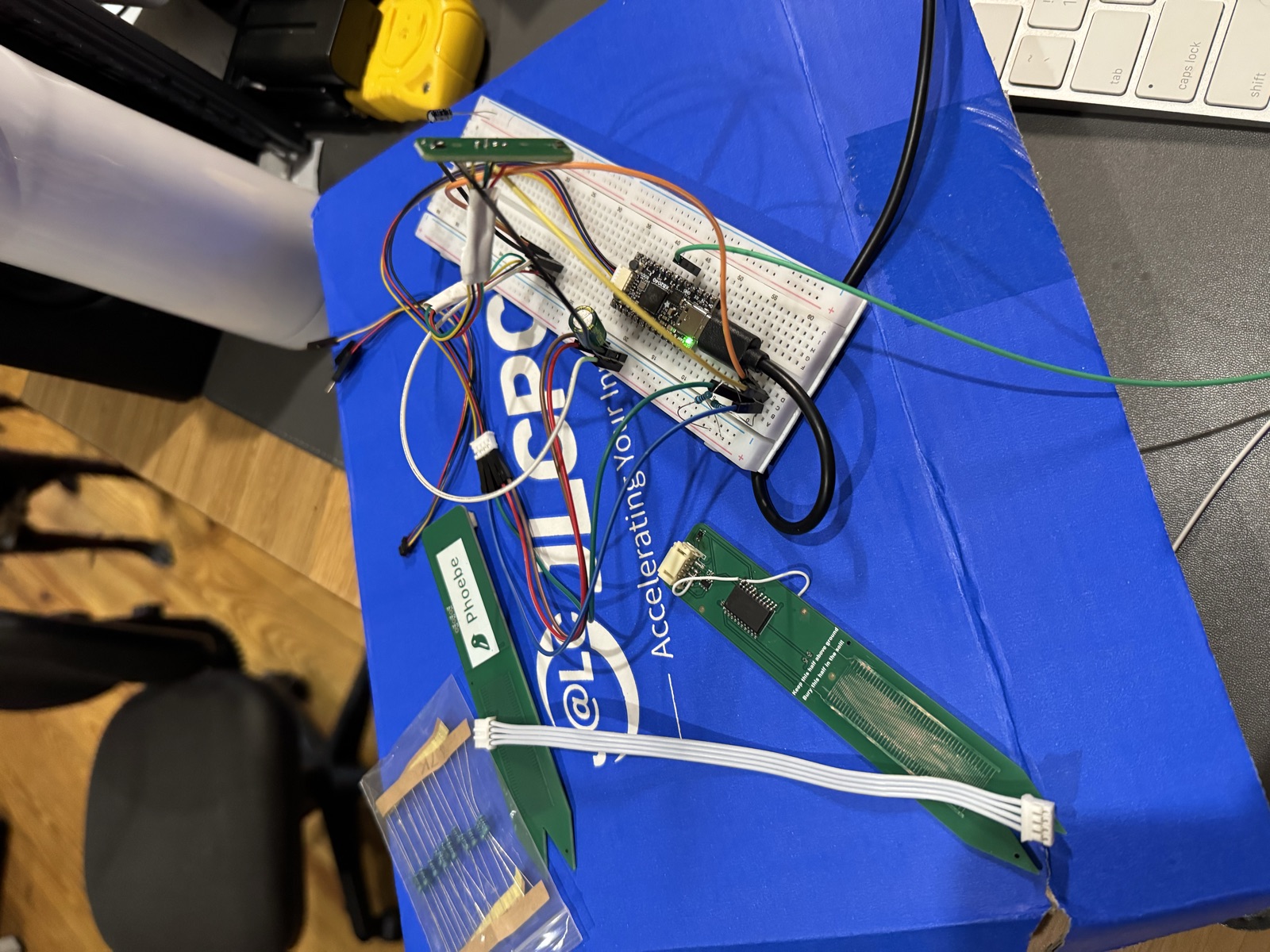 Overhead view of the bench with a few Prong boards laid out and the Head board wired into a breadboard, all on the blue JLCPCB box