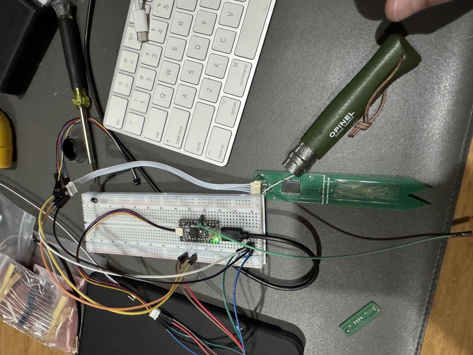 Breadboard bench setup with a dev board, ribbon cable to the Prong, and an Opinel knife used as a pointer